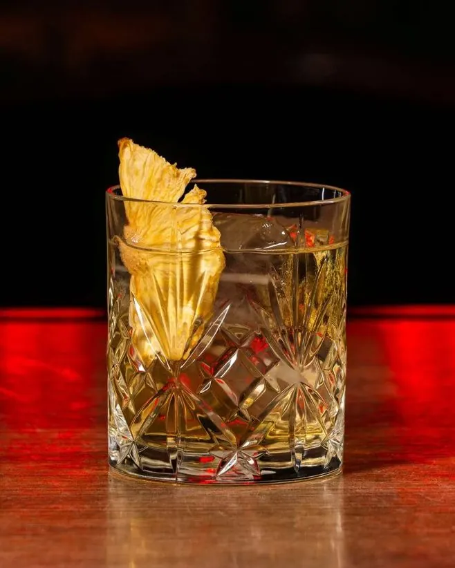 Cóctel con piña en vaso tallado bajo el neón de Bloody Zaragoza