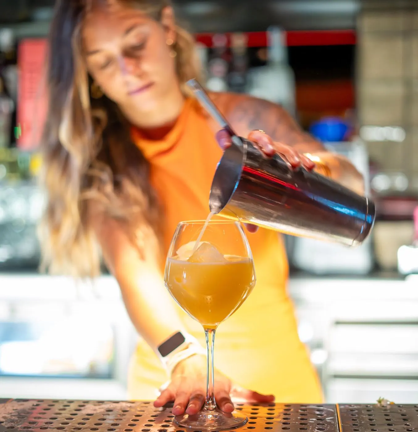 Bartender sirviendo un cóctel de naranja en copa